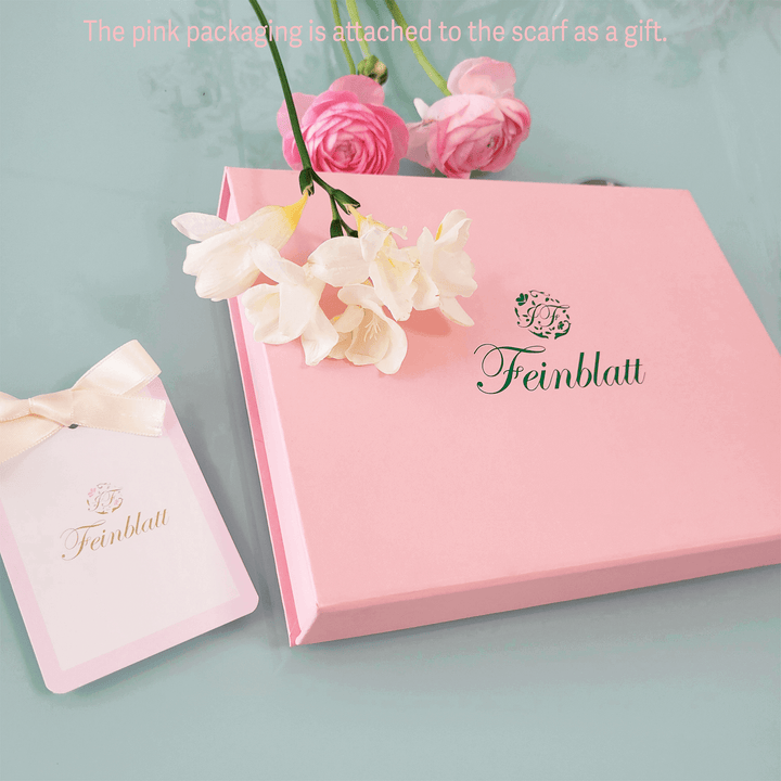 Eine elegante Geschenkverpackung in Rosa mit Feinblatt-Logo und zarten Blumen, daneben eine Geschenkkarte mit Schleife  eine stilvolle Präsentation für den hochwertigen Designer-Seidenschal von  Feinblatt