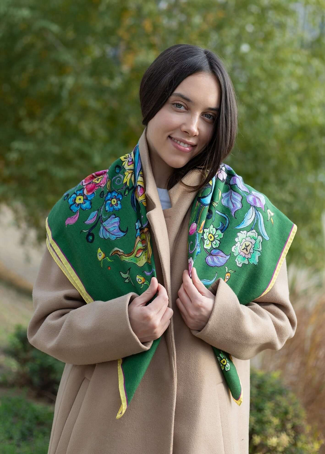 Model wearing a green designer cashmere butterfly shawl with floral patterns, showcasing elegance outdoors.
