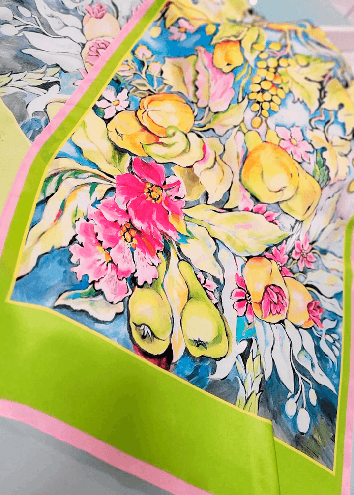 Detailaufnahme eines handgemalten Designer-Seidenschals mit farbenfrohem Obst und Blütenmotiv in Gelb, Pink, Grün und Blau auf Seidensatin – hochwertiges Sommeraccessoire von Iryna Feinblatt