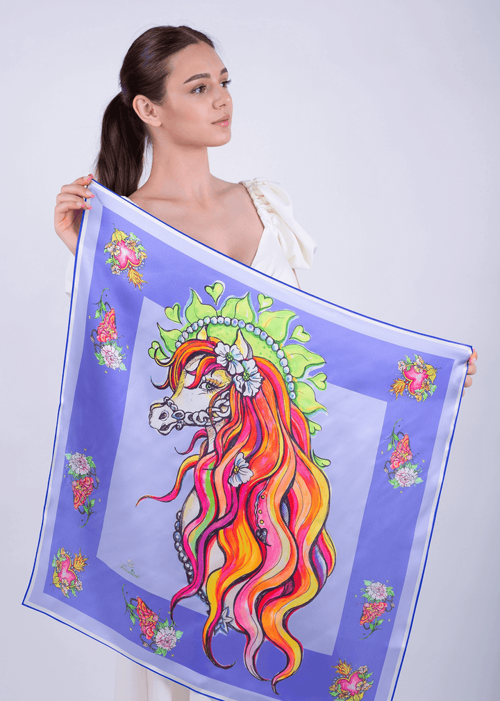 Model showcasing a designer silk scarf with vibrant blue colors and a floral horse design.