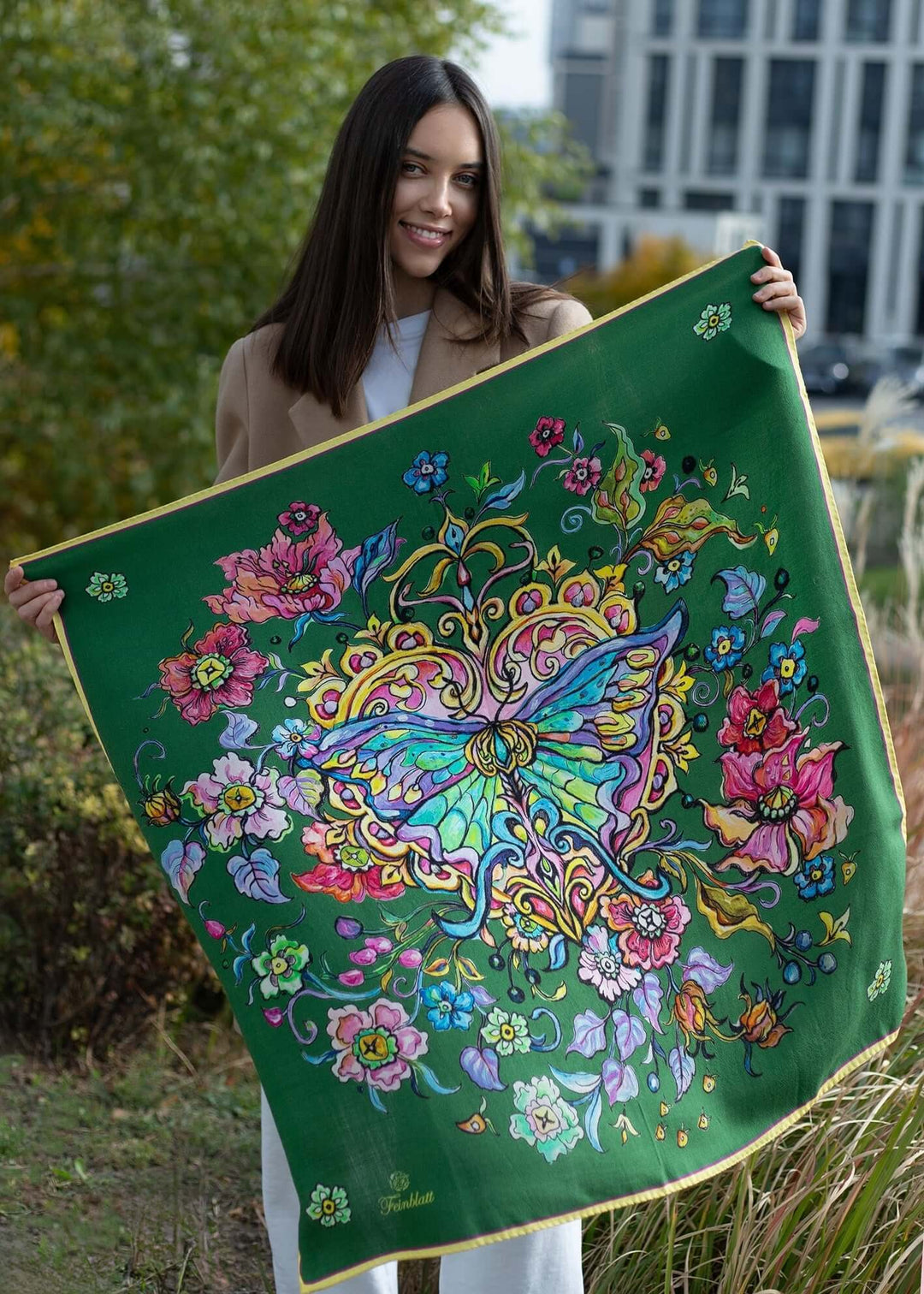 Woman holding a green designer cashmere scarf with a butterfly and floral pattern, showcasing elegance and style.