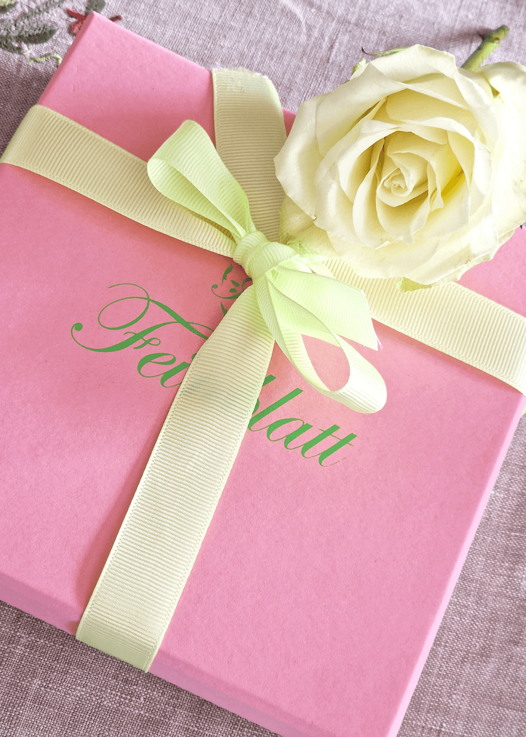 Geschenkverpackung von Feinblatt: Rosafarbene Box mit zartgrüner Schleife und weißer Rose