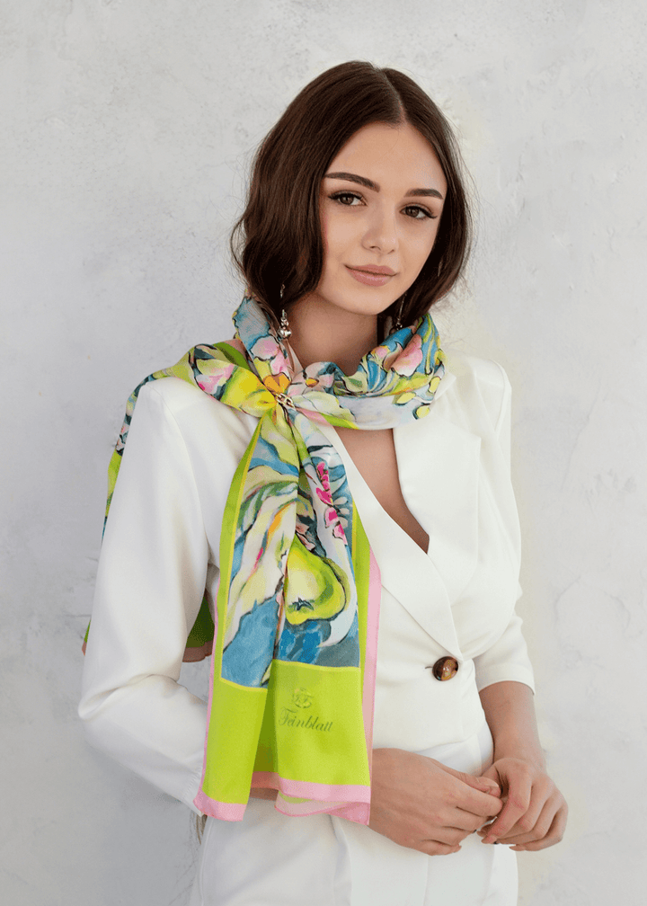 Elegantes Designer Seidenschal mit farbenfrohem Sommerblumenmuster in Grün, Blau und Rosa, von einer stilvollen Frau im weißen Blazer getragen – exklusives Designer-Accessoire von Iryna Feinblatt