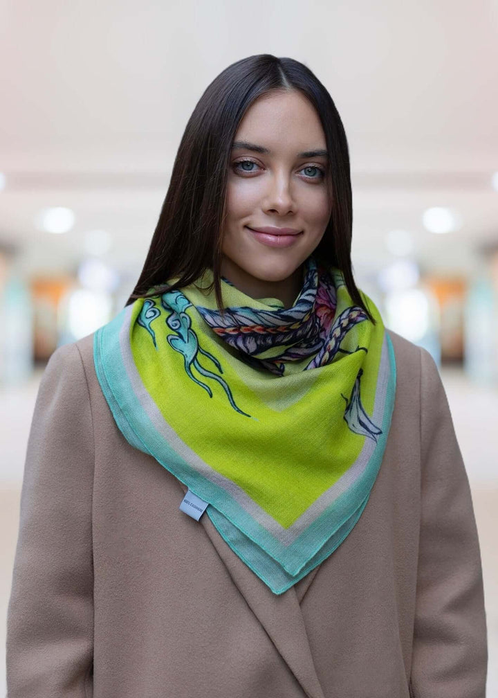 Model wearing a yellow designer cashmere scarf with dragon design, featuring a vibrant green background.