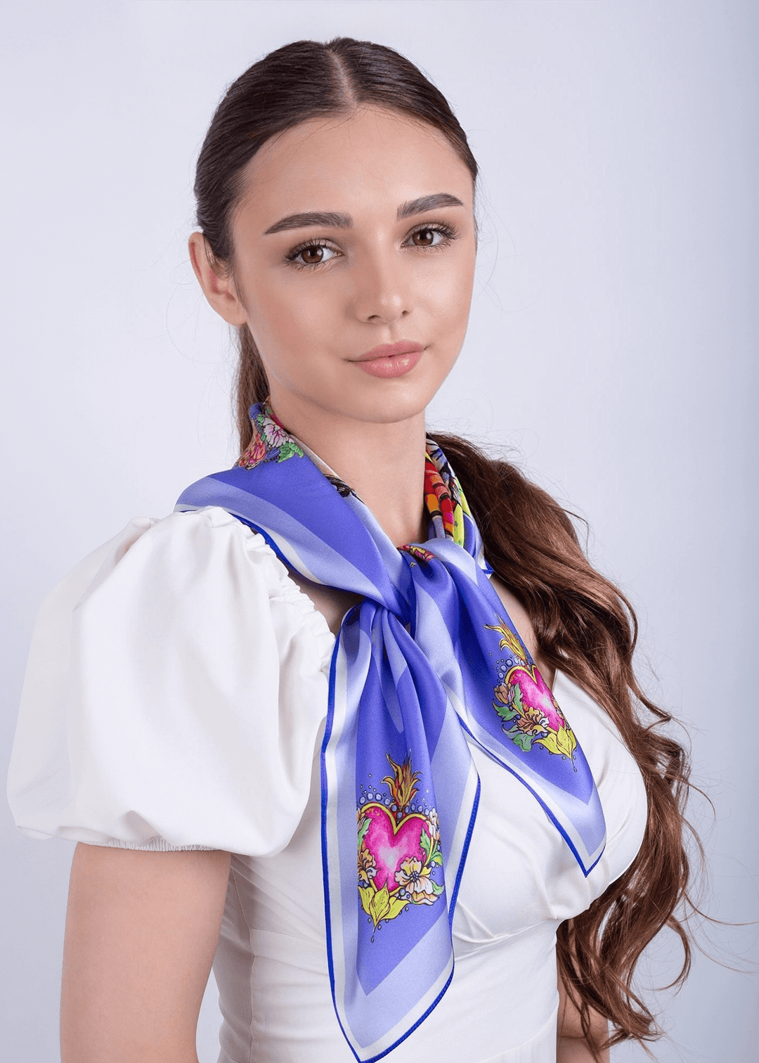 Model wearing a designer silk scarf in blue with floral and heart patterns, showcasing a chic fashion accessory.