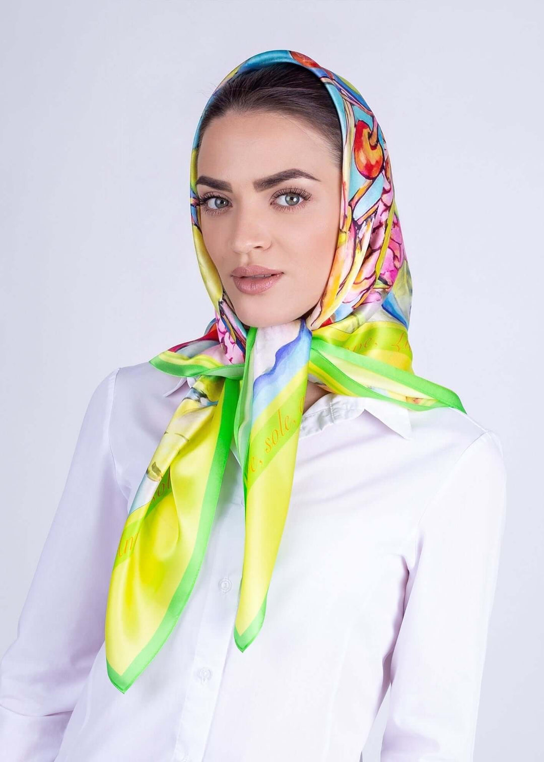 Elegant woman wearing a colorful silk scarf with bird motifs, showcasing vibrant yellow and green shades.