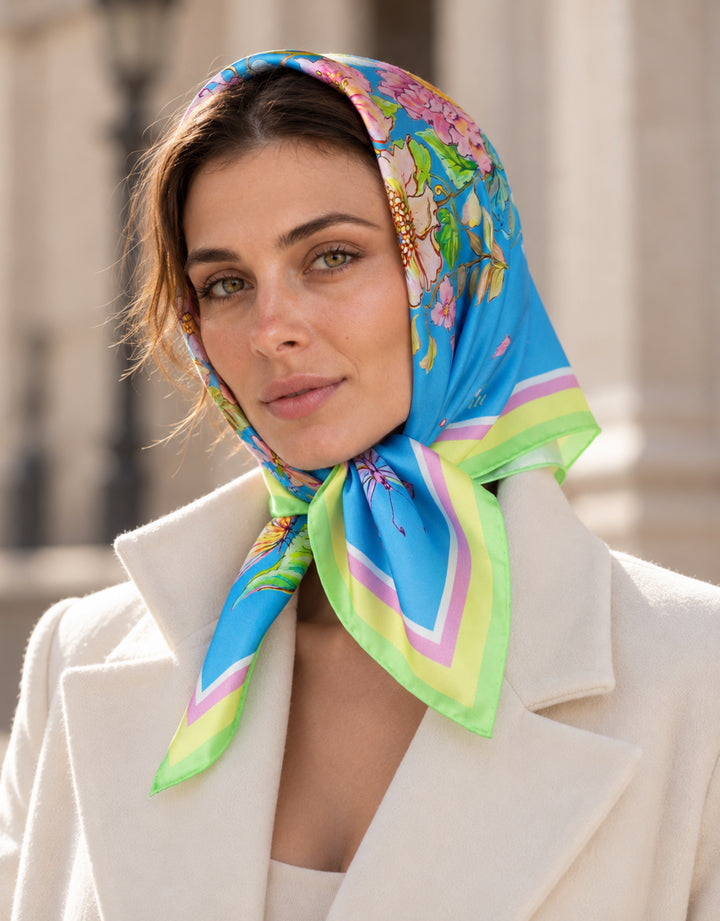 Frau trägt einen blauen Designer-Seidenschal von Feinblatt mit Blumenmuster als Kopftuch, unter dem Kinn gebunden.