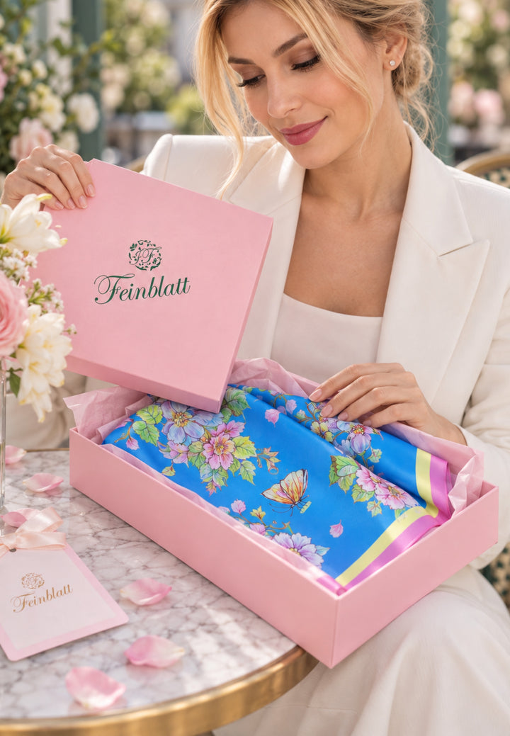 Blauer Designer-Seidenschal von Feinblatt mit floralem Kunstmotiv in einer rosa Geschenkbox.
