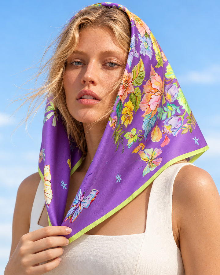 Ein Kopftuch aus Seidentwill in der Farbe Blue Violet mit den Maßen 65 × 65 cm, elegant um den Kopf gebunden, ziert den Kopf der Blondine.