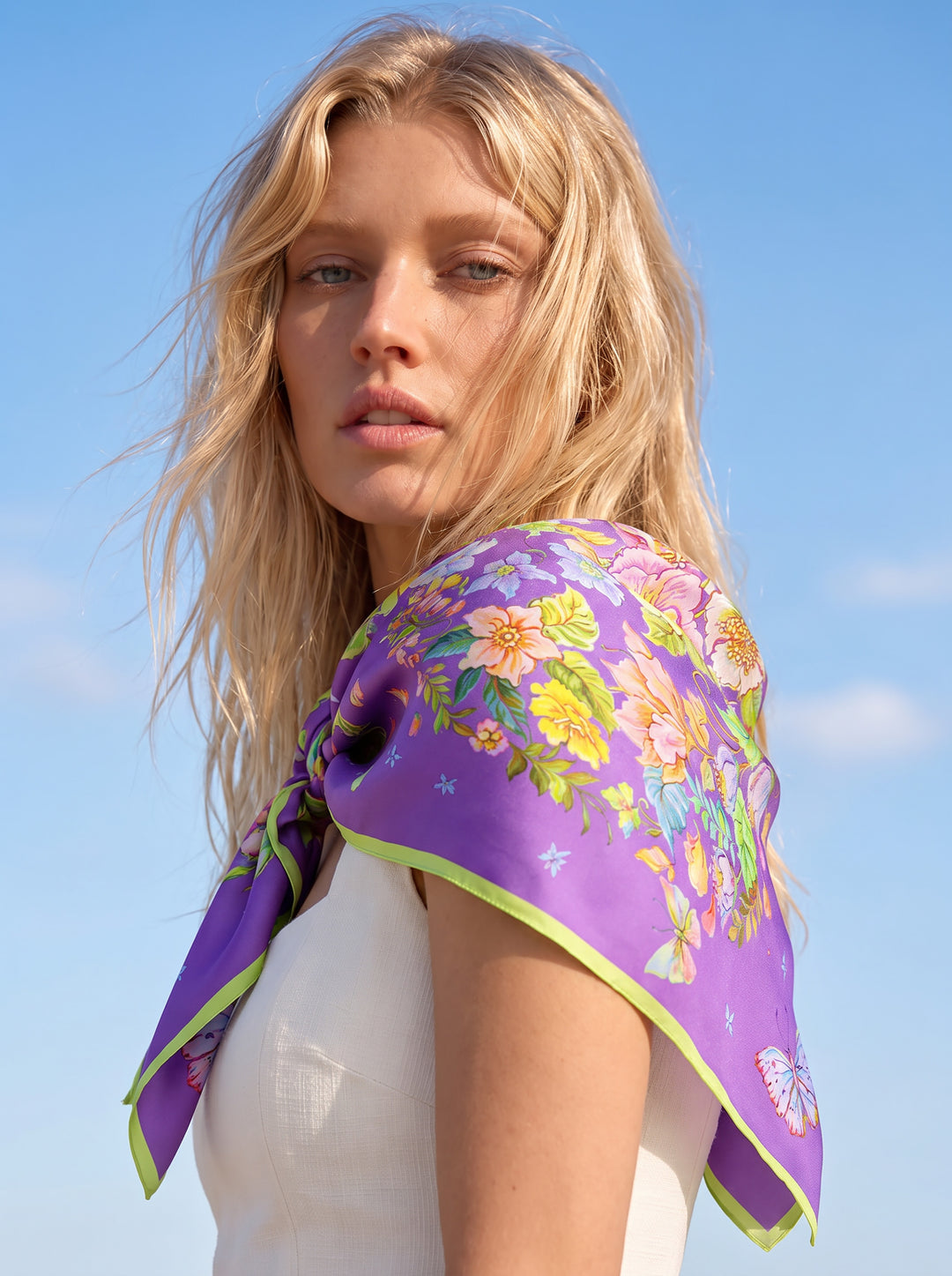Eine blonde Frau im hellen Sommerkleid, seitlich stehend, hat das Seidentuch Blue Violet aus Seidentwill elegant über die Schultern gelegt.