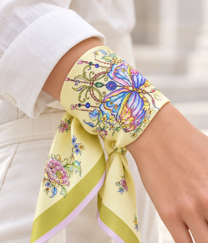 Gelber Seidenschal von Feinblatt mit Schmetterling und Blumenmuster, als Armband um das Handgelenk gebunden.