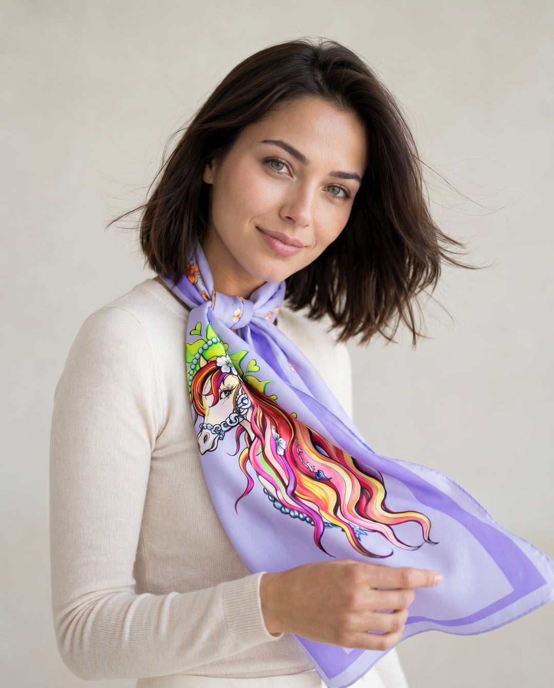 Elegant woman wearing Pretty in Blue designer silk scarf with colorful fantasy horse illustration and soft lilac tones in minimalist studio setting.
